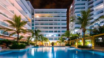 Un hotel moderno con piscina, palmeras y una fachada bien iluminada.