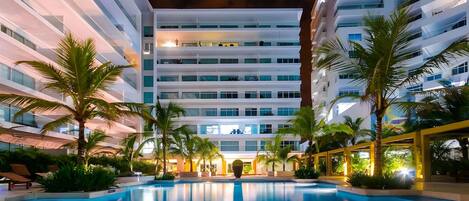 Un hôtel moderne doté d’une piscine, de palmiers et d’une façade bien éclairée.