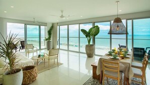 A spacious living area with a large window overlooking the beach, a dining table set for two, and a ceiling fan. - Condominio frente al mar  Morros Epic. (Cartagena)