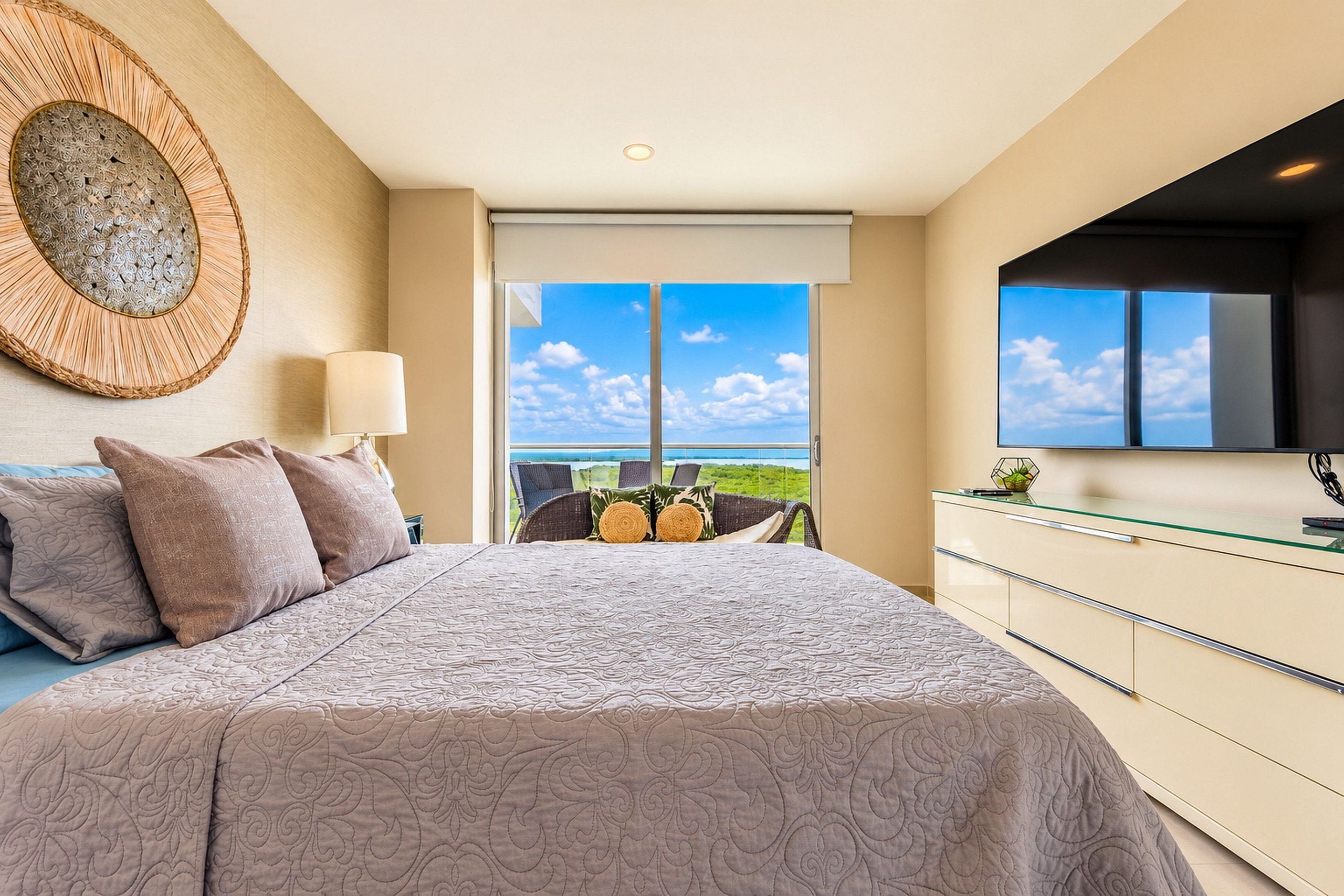 Un dormitorio con una cama grande, vistas al cielo y al verdor, un televisor montado en la pared y un moderno aparador.