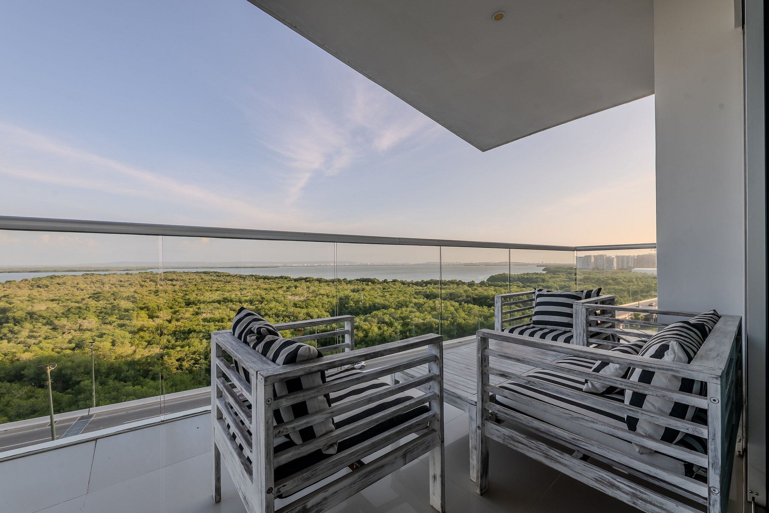A balcony with white wooden furniture and a view of a green landscape and city skyline.