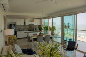 A modern kitchen with white cabinets, a dining area with a table and chairs, and large windows overlooking a beach. - Condominio frente al mar  Morros Epic. (Cartagena)
