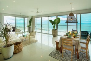 A spacious living area with a large window overlooking the beach, a dining table set for two, and a ceiling fan. - Condominio frente al mar  Morros Epic. (Cartagena)