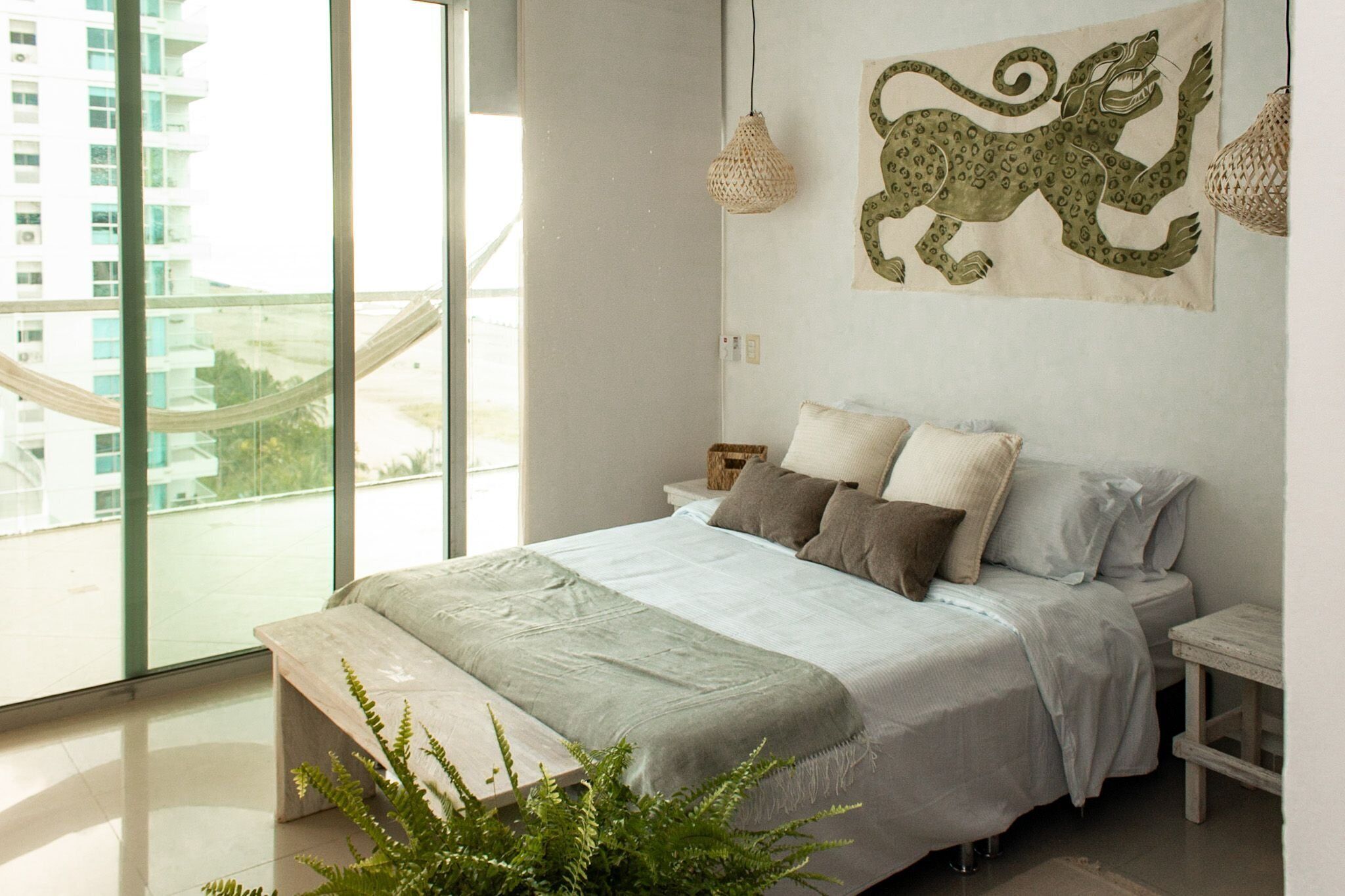 A modern bedroom with a large bed, a view of a cityscape through a large window, and a decorative tapestry on the wall.