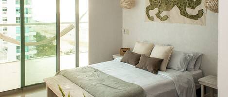 A modern bedroom with a large bed, a view of a cityscape through a large window, and a decorative tapestry on the wall.