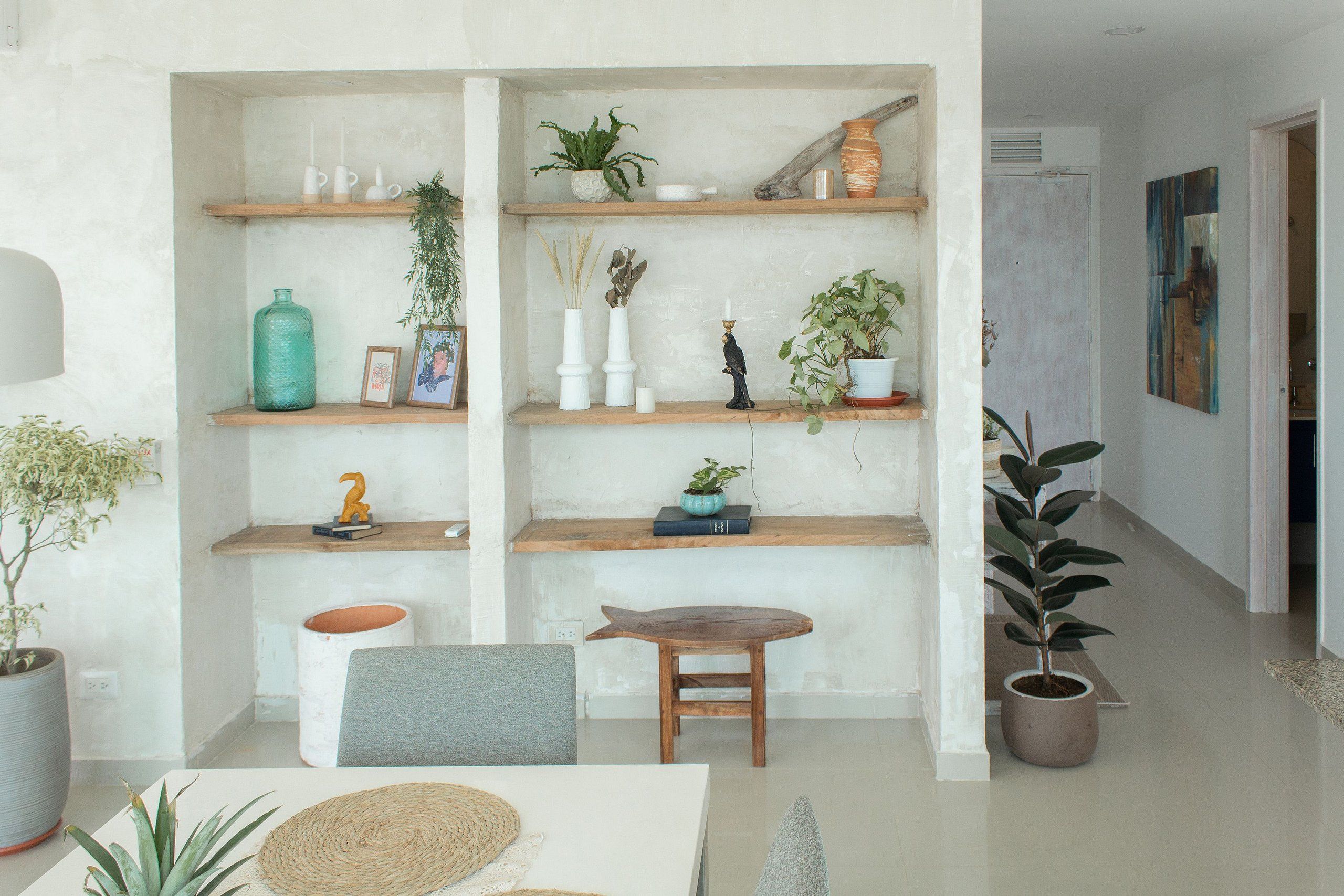Un soggiorno moderno con una panca in legno, un tavolo da pranzo e una libreria piena di oggetti decorativi e piante.