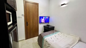 A bedroom with a bed, a television, a wooden door, and a microwave.