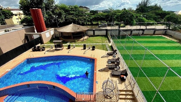 A rooftop swimming pool with a diving board, surrounded by lounge chairs and a grassy area.