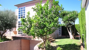 A building with a pink facade, large windows, and a well-maintained garden with various trees and a grassy lawn. - Villa Berria (Marratxí)
