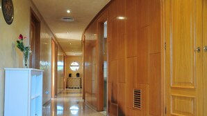 A hallway with wooden paneling, a white console table with a vase of flowers, and a polished floor. - Villa Berria (Marratxí)