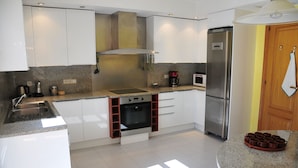 A modern kitchen with white cabinets, a stainless steel refrigerator, a built-in oven, and a granite countertop. - Villa Berria (Marratxí)