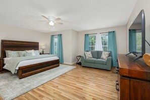 Une chambre à coucher avec un lit en bois, un canapé gris, une commode en bois et un ventilateur de plafond.