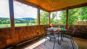 Une terrasse couverte avec une table et des chaises en bois, un tapis à motifs et une vue sur un paysage verdoyant.