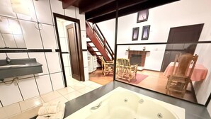 A bathroom with a bathtub, a sink, and a mirror. There is a wooden staircase leading to a dining area with chairs and a table. - Pousada Sol Nascente (Camanducaia)