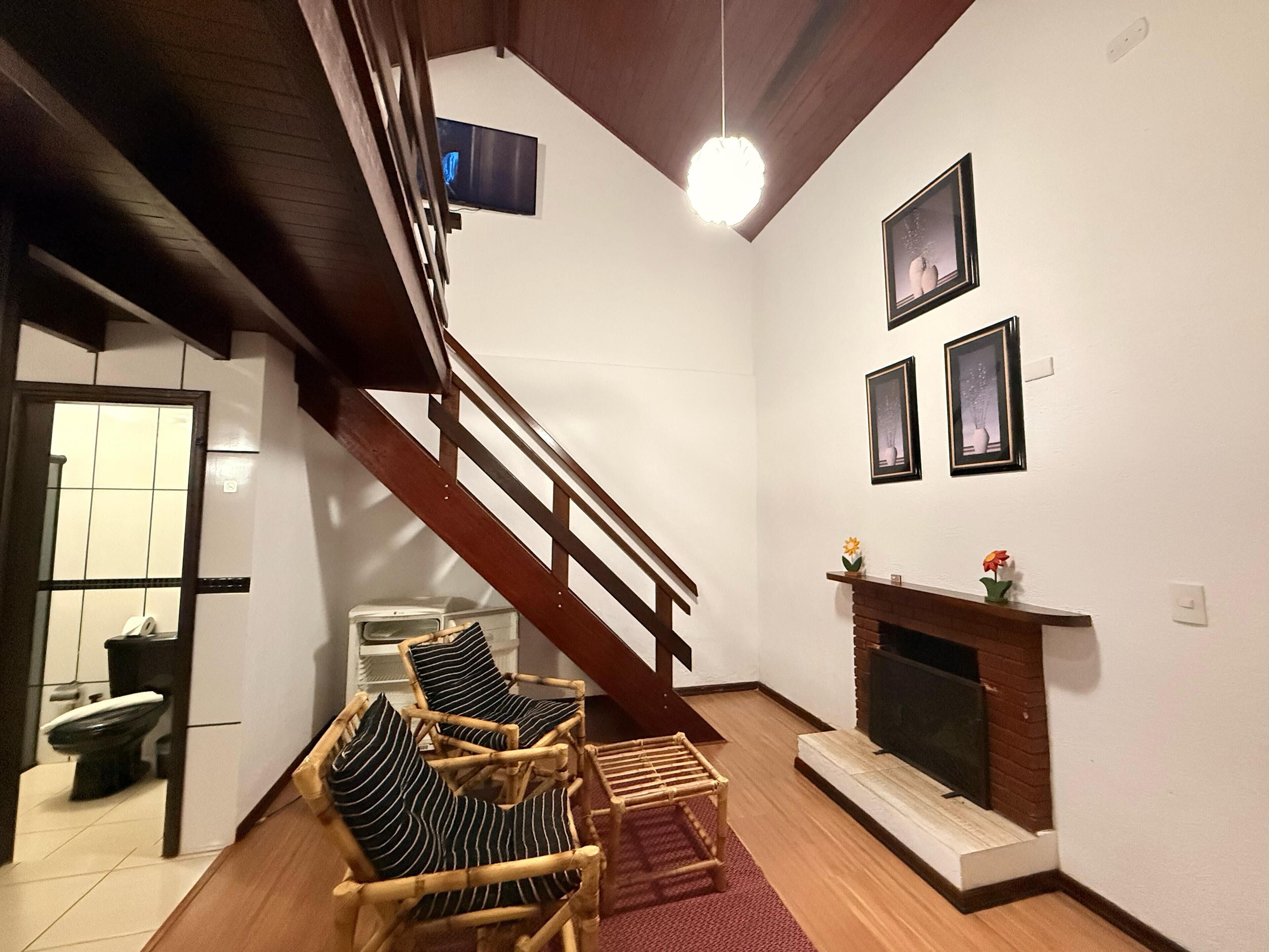 A living room with a wooden staircase, a fireplace, and a dining area with a table and chairs.
