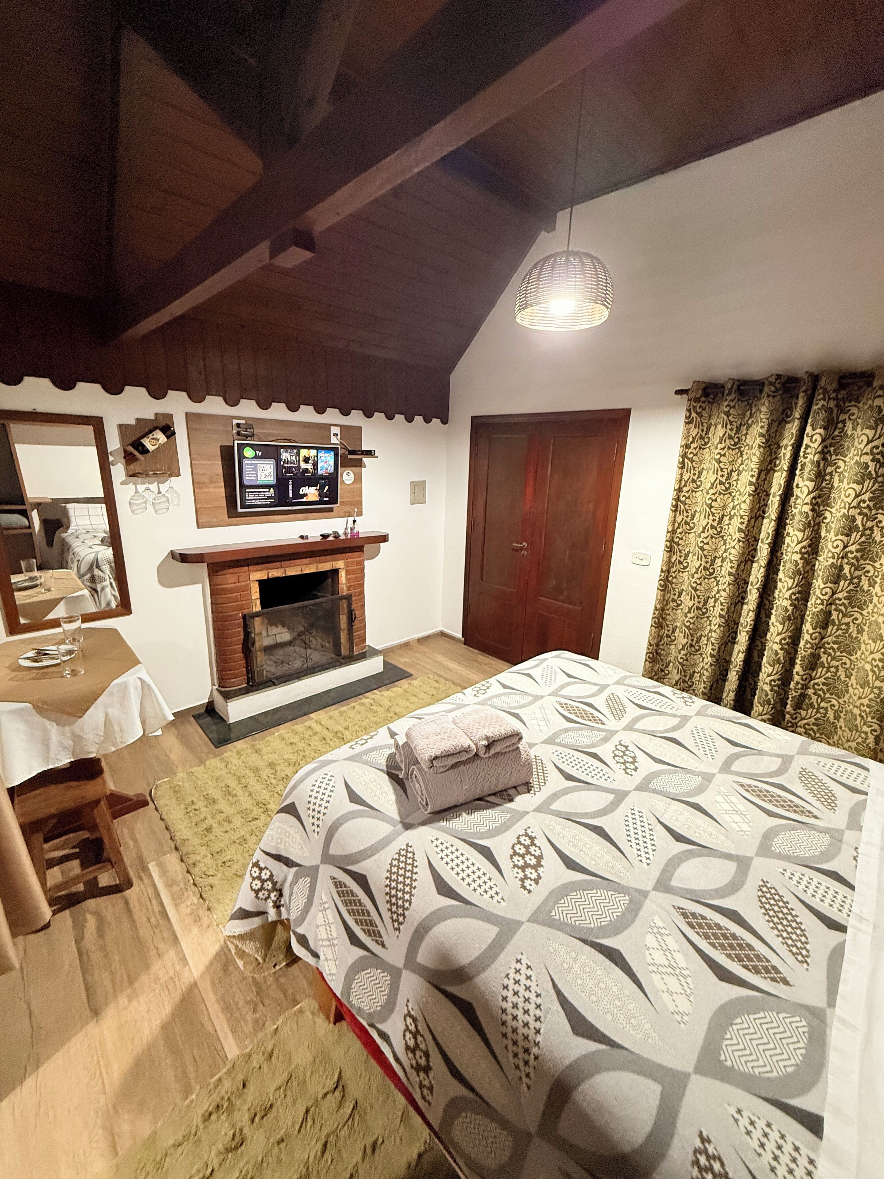 A bedroom with a bed, a fireplace, a television, and a wooden ceiling.