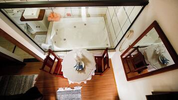A high-ceilinged bathroom with a large bathtub, a mirror, and a wooden floor.