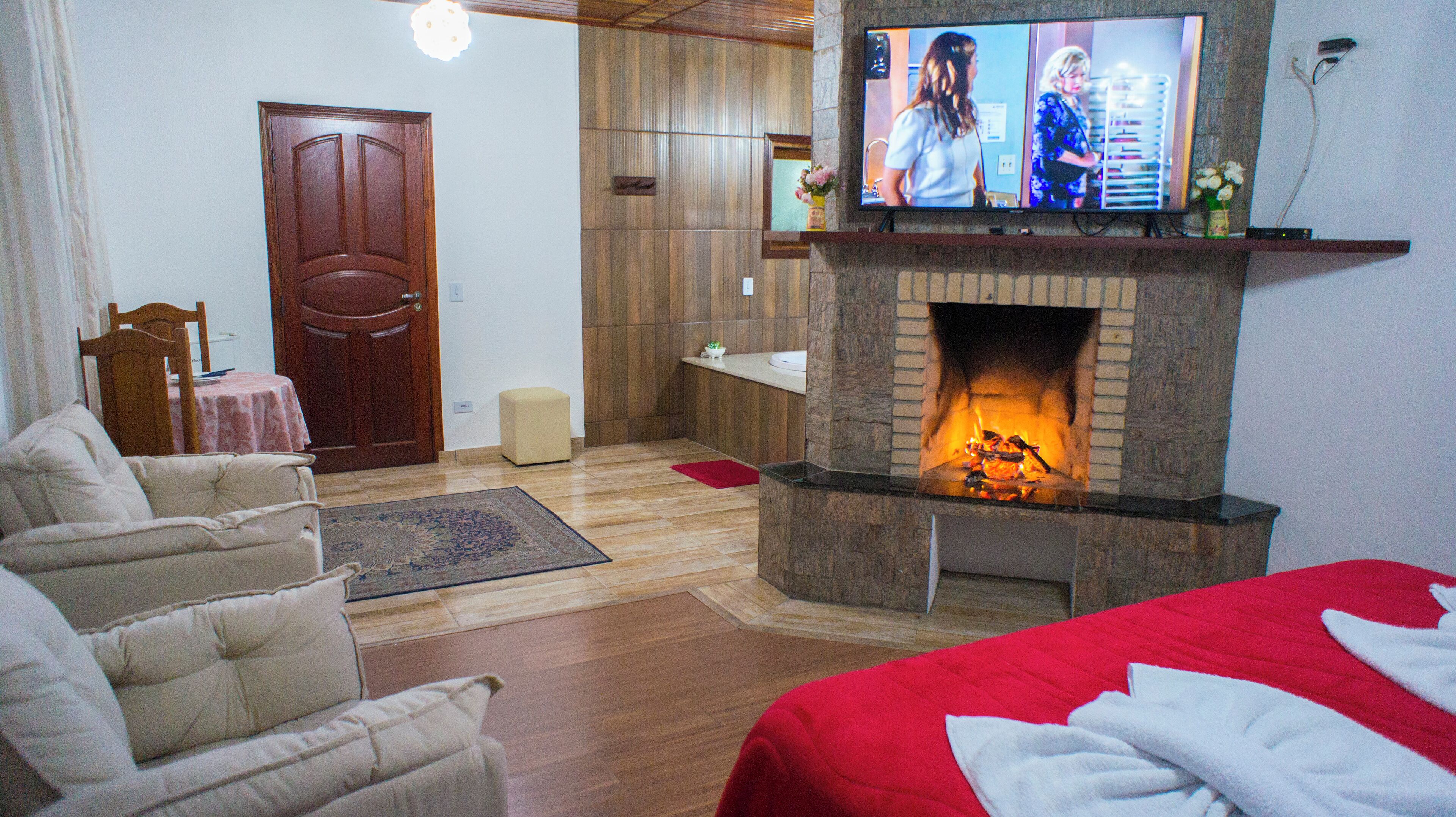 A living room with a fireplace, a television mounted above it, a sofa, a red blanket, and a wooden door.