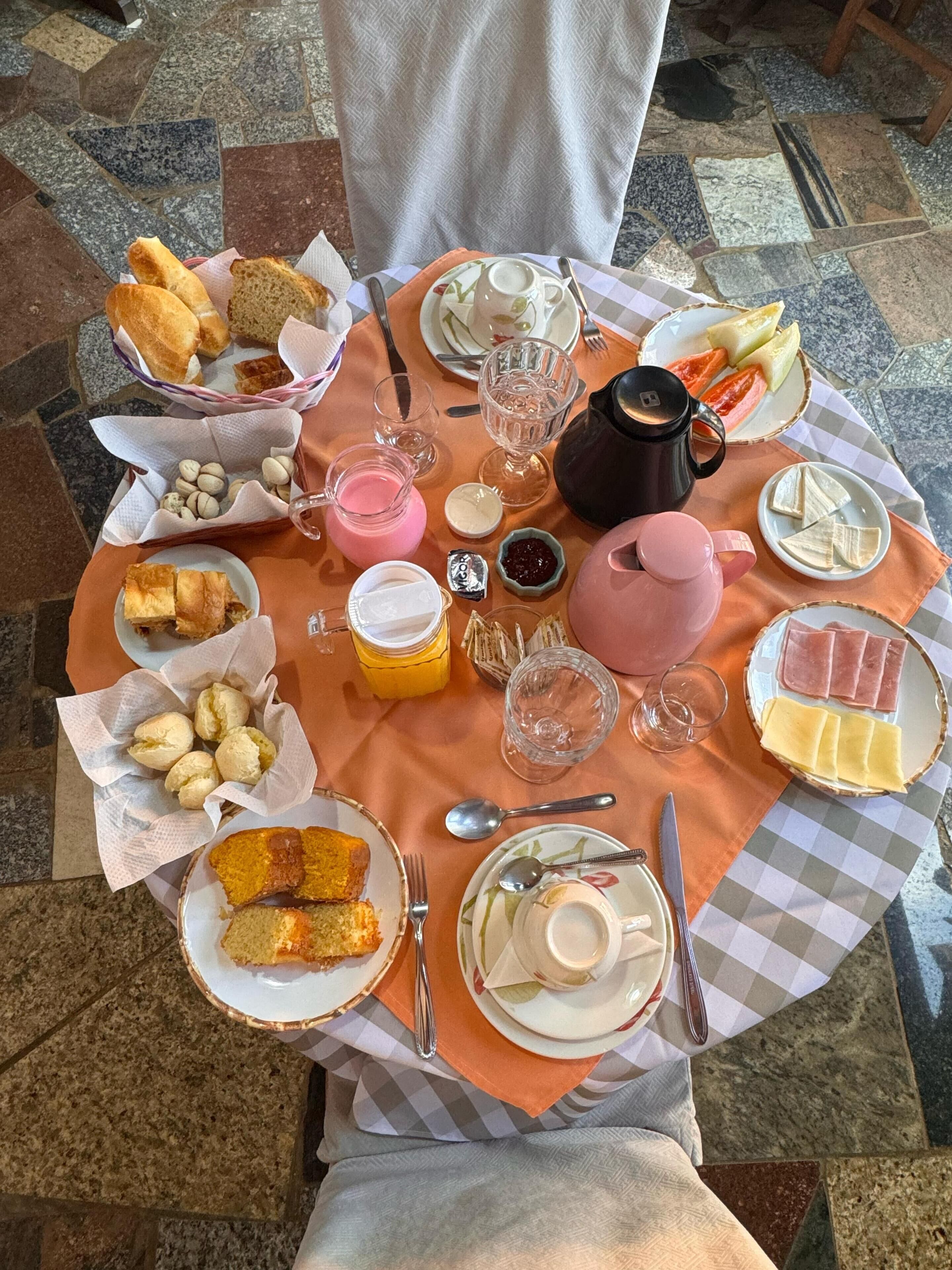 Et rundt bord med et udvalg af mad, herunder brød, kager, ost og nødder, samt flere kopper og en tepotte.