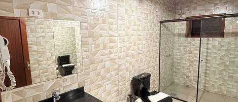 A modern bathroom with a geometric tile backsplash, a black sink, a toilet, and a glass-enclosed shower.