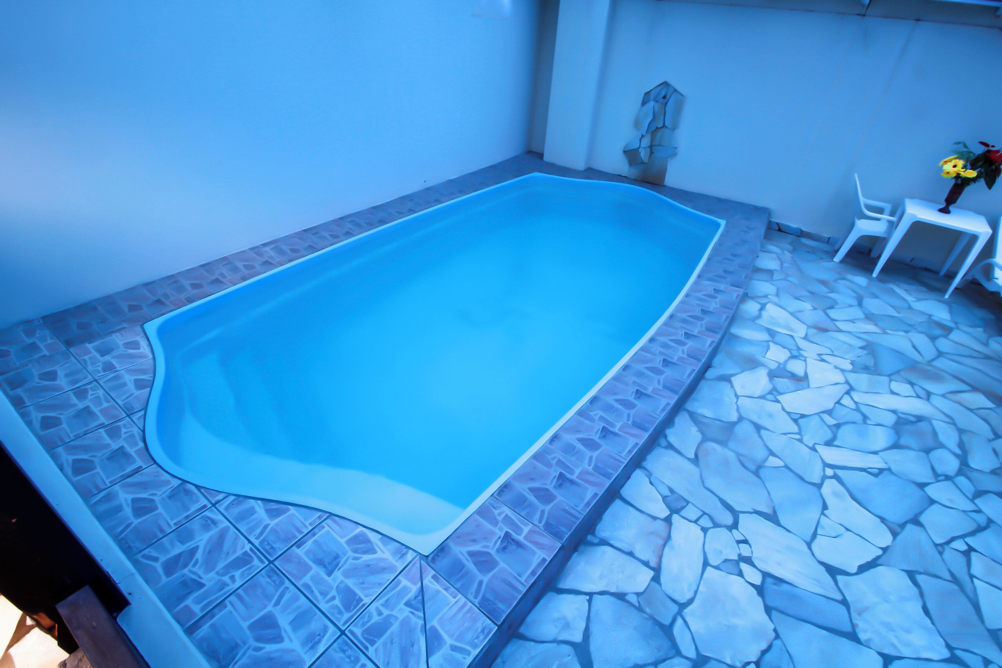 A rectangular swimming pool with a stone border, surrounded by a stone patio.