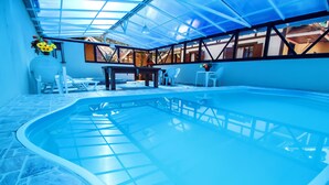 An indoor swimming pool with a glass ceiling, surrounded by white chairs and a table. - Pousada Sol Nascente (Camanducaia)