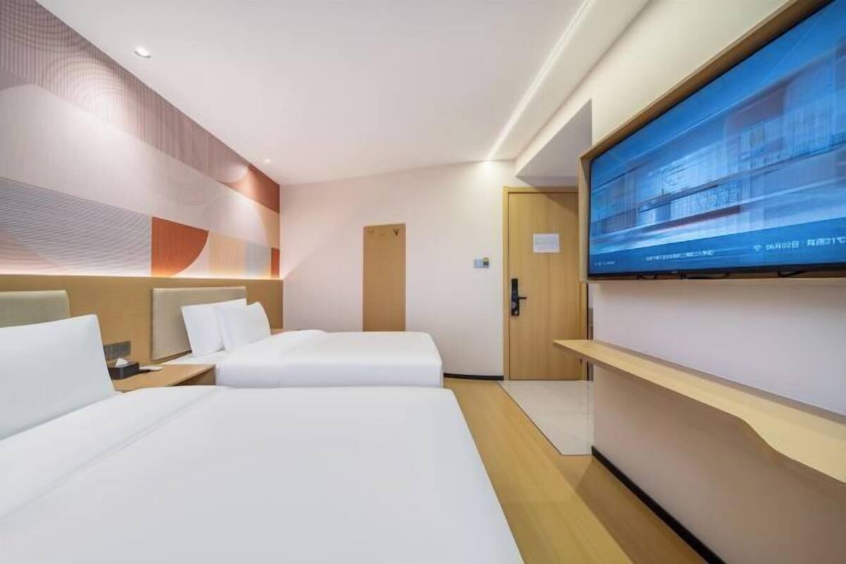 Una habitación de hotel con dos camas, un televisor en la pared y una puerta de madera.