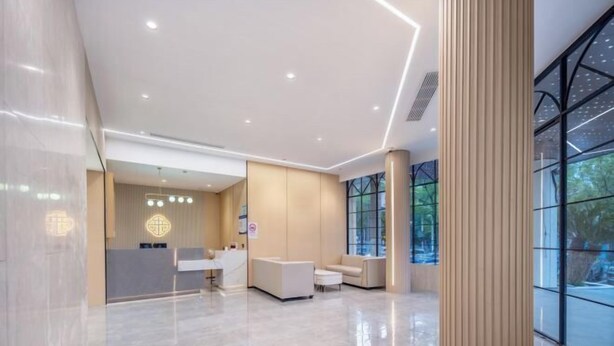 Eine moderne Hotelhalle mit einer Rezeption, einer Sitzecke und großen Fenstern mit Blick ins Freie.