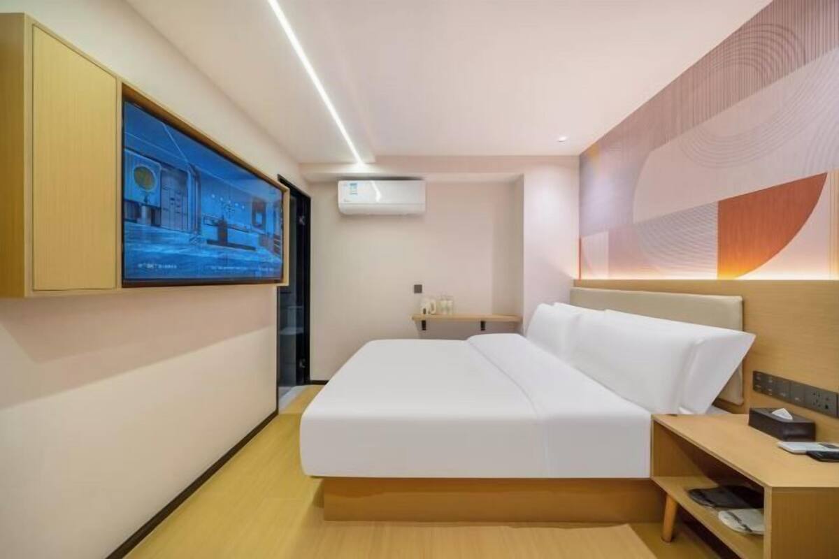 Una habitación de hotel moderna con cama, mesita de noche y televisor montado en la pared.