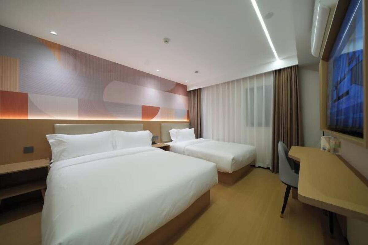 Habitación de hotel con dos camas, un escritorio y un ventanal grande con cortinas.