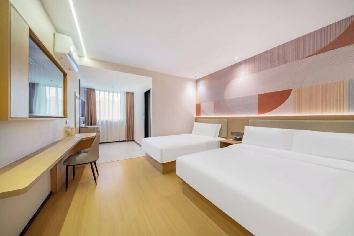 Habitación de hotel con escritorio, dos camas, un espejo y vistas al pasillo.