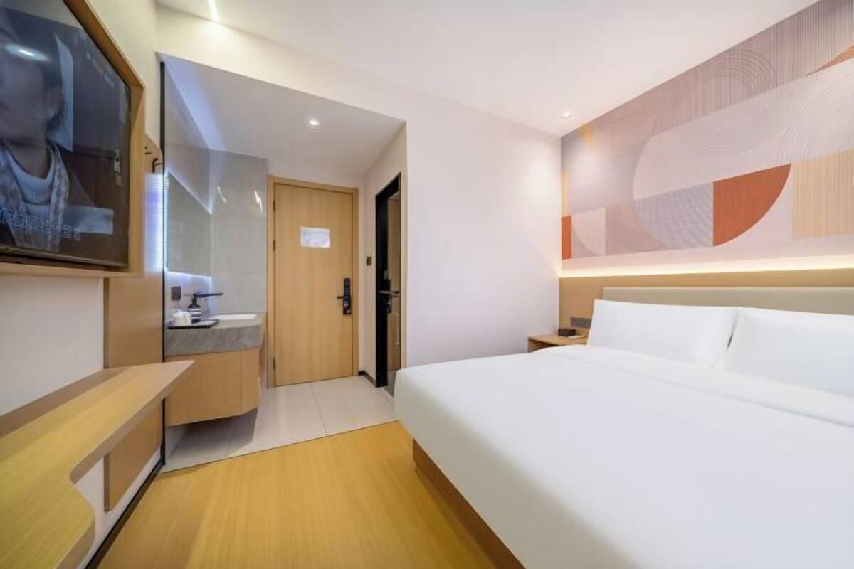 Una habitación de hotel con cama, escritorio, espejo, televisor y baño.