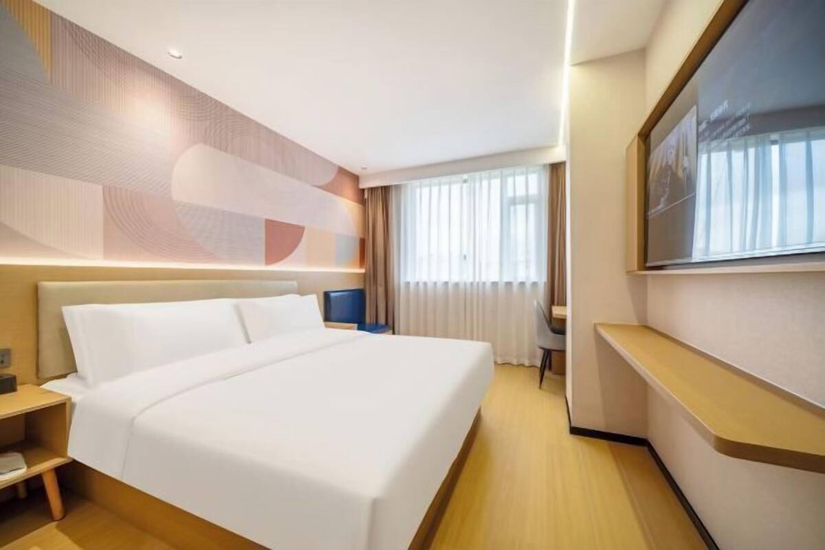 Habitación de hotel con una cama grande, un escritorio, una silla, un televisor y una ventana con cortinas.