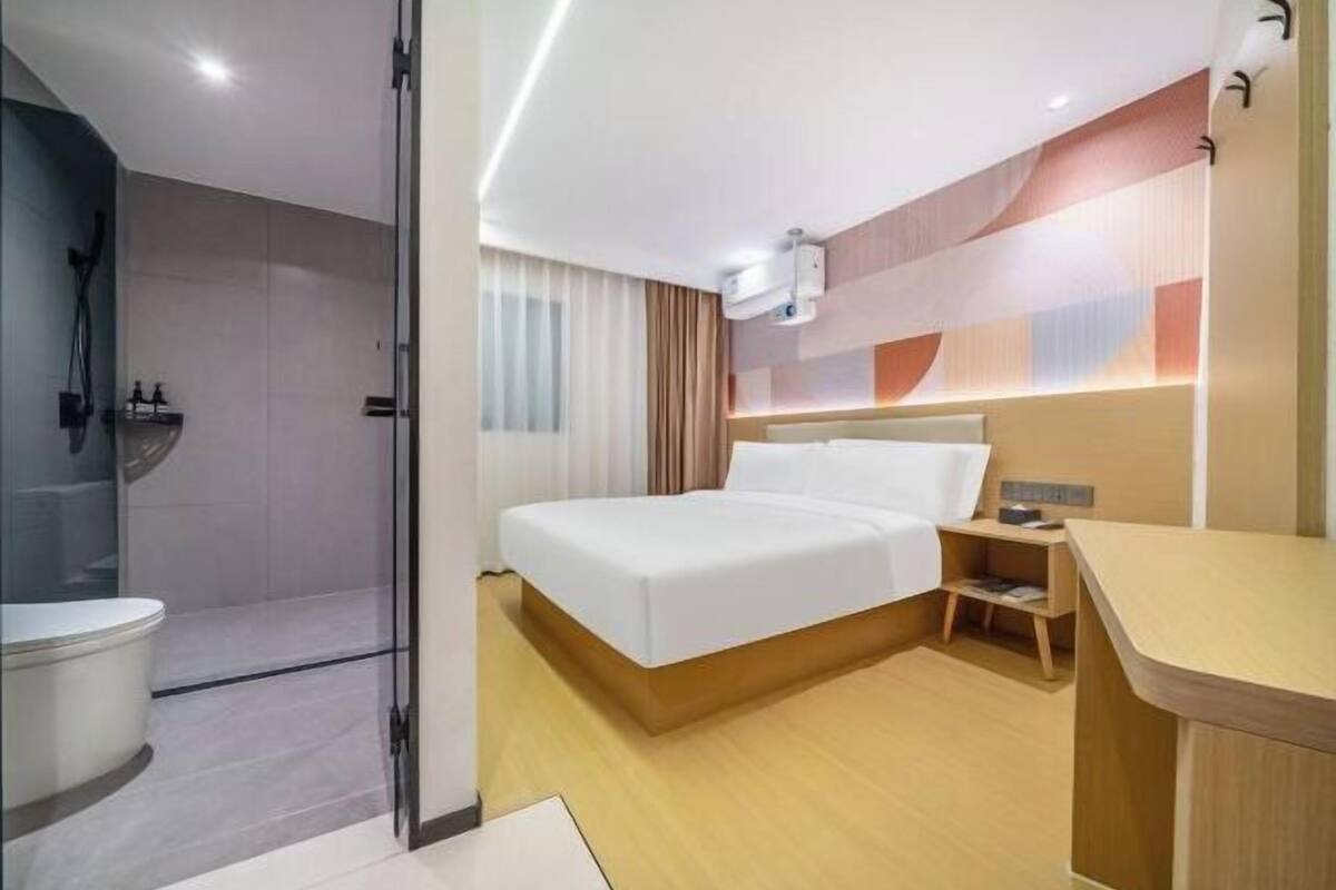 Una habitación de hotel moderna con una cama grande, zona de ducha separada y una mesita de noche pequeña.