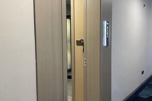 Un pasillo con una puerta cerrada, un interruptor de luz y un cartel en la pared.