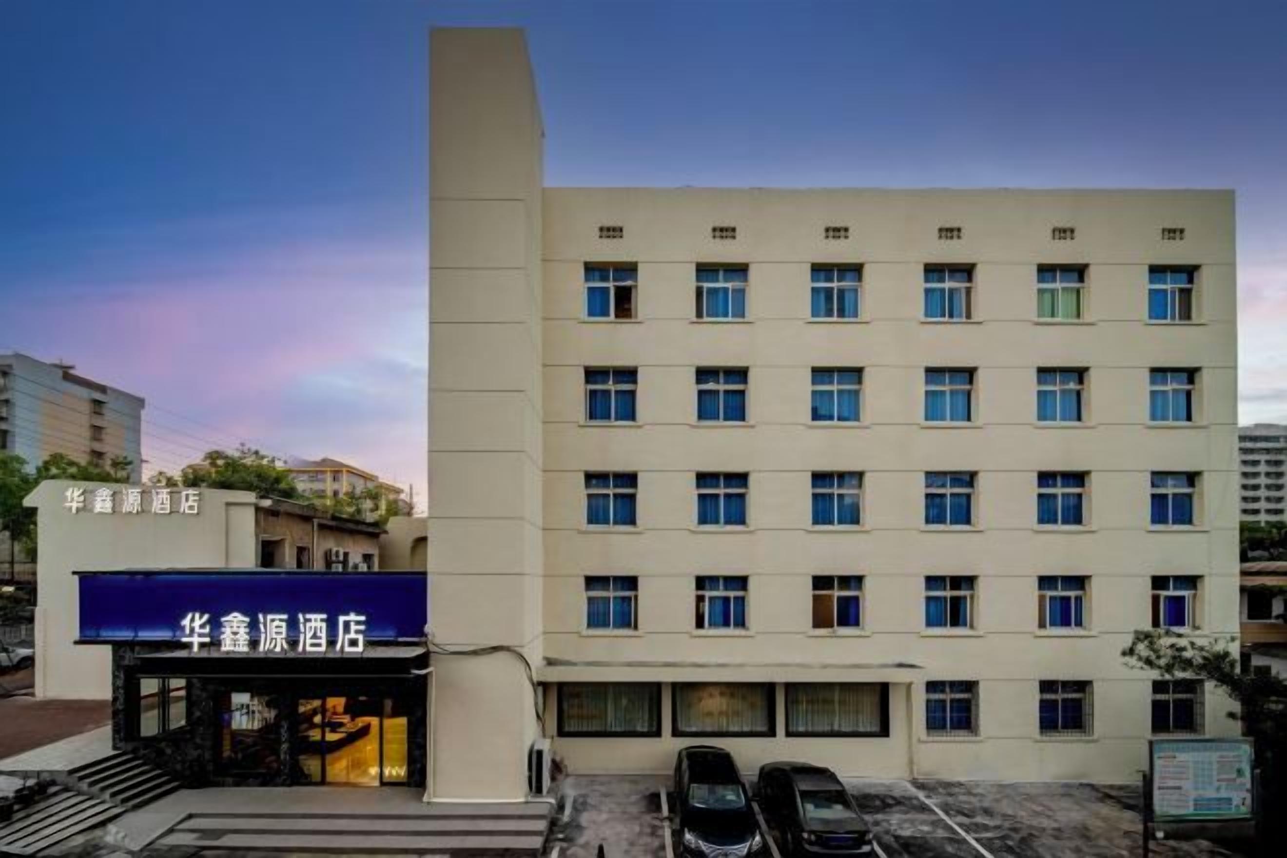 A multi-story hotel building with a flat facade, multiple windows, and a parking area in front.