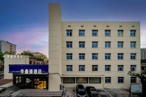 A multi-story hotel building with a flat facade, multiple windows, and a parking area in front. - Huaxinyuan Hotel (Yiyang)