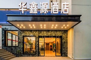 Entrada de hotel con un cartel sobre las puertas, una zona de acceso cubierta y una escalera que lleva a la entrada.