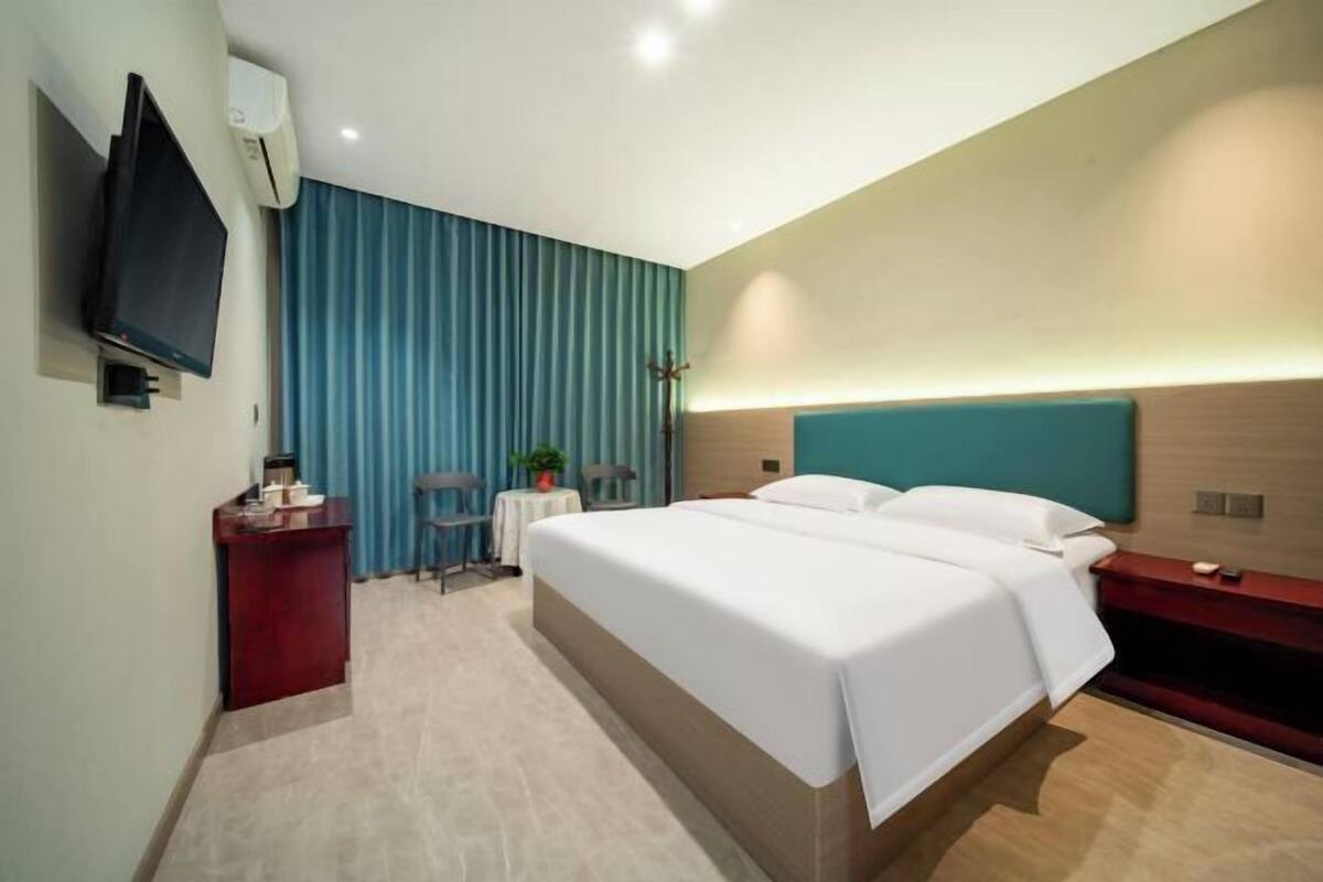 Una habitación de hotel moderna con una cama grande, un escritorio, un televisor y una ventana con cortinas.