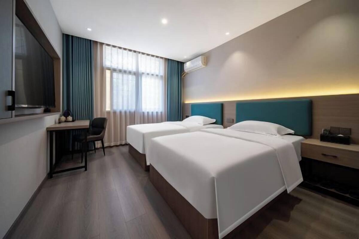 Habitación de hotel con dos camas, un escritorio, una silla, un televisor y una ventana con cortinas.
