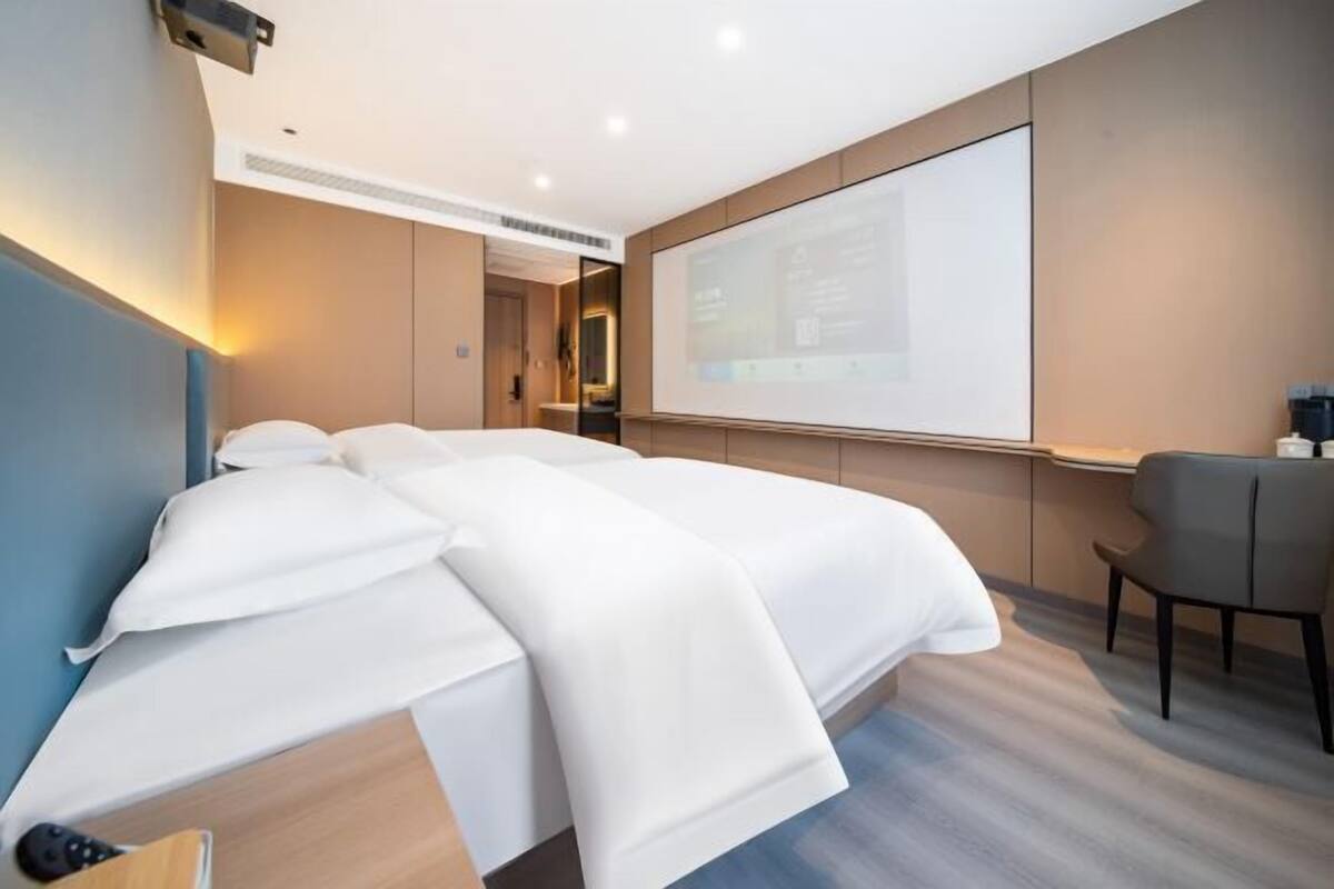 Una habitación de hotel moderna con una cama grande, un escritorio y una pantalla para proyector en la pared.