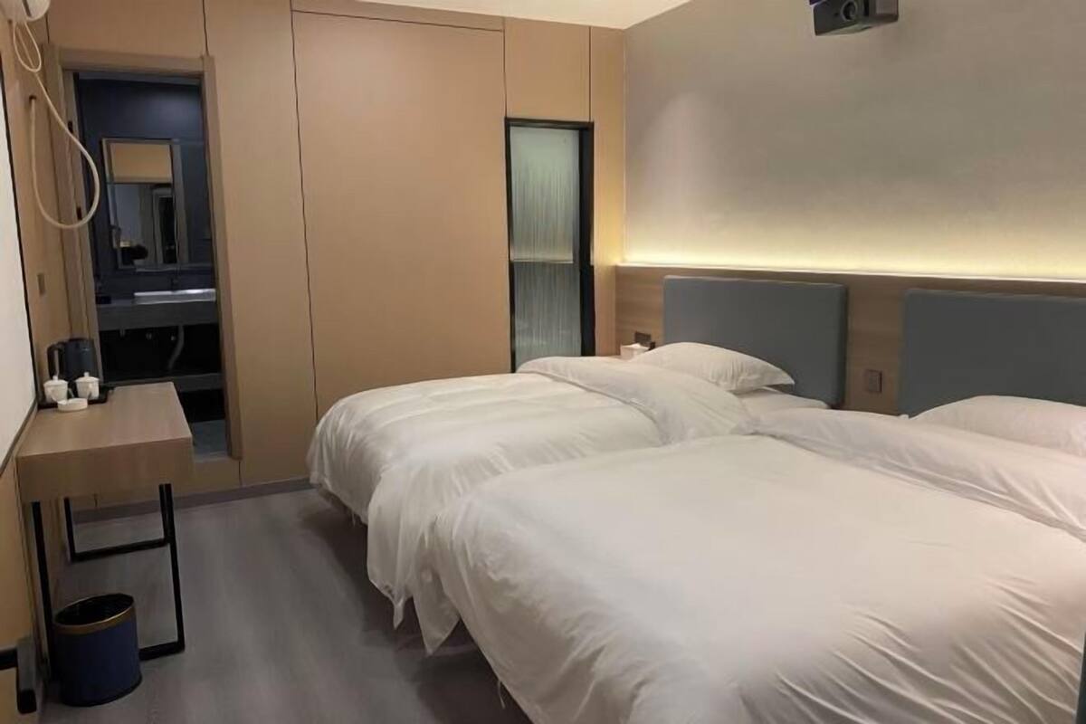 Habitación de hotel con dos camas, un escritorio, un espejo y una lámpara fijada en la pared.