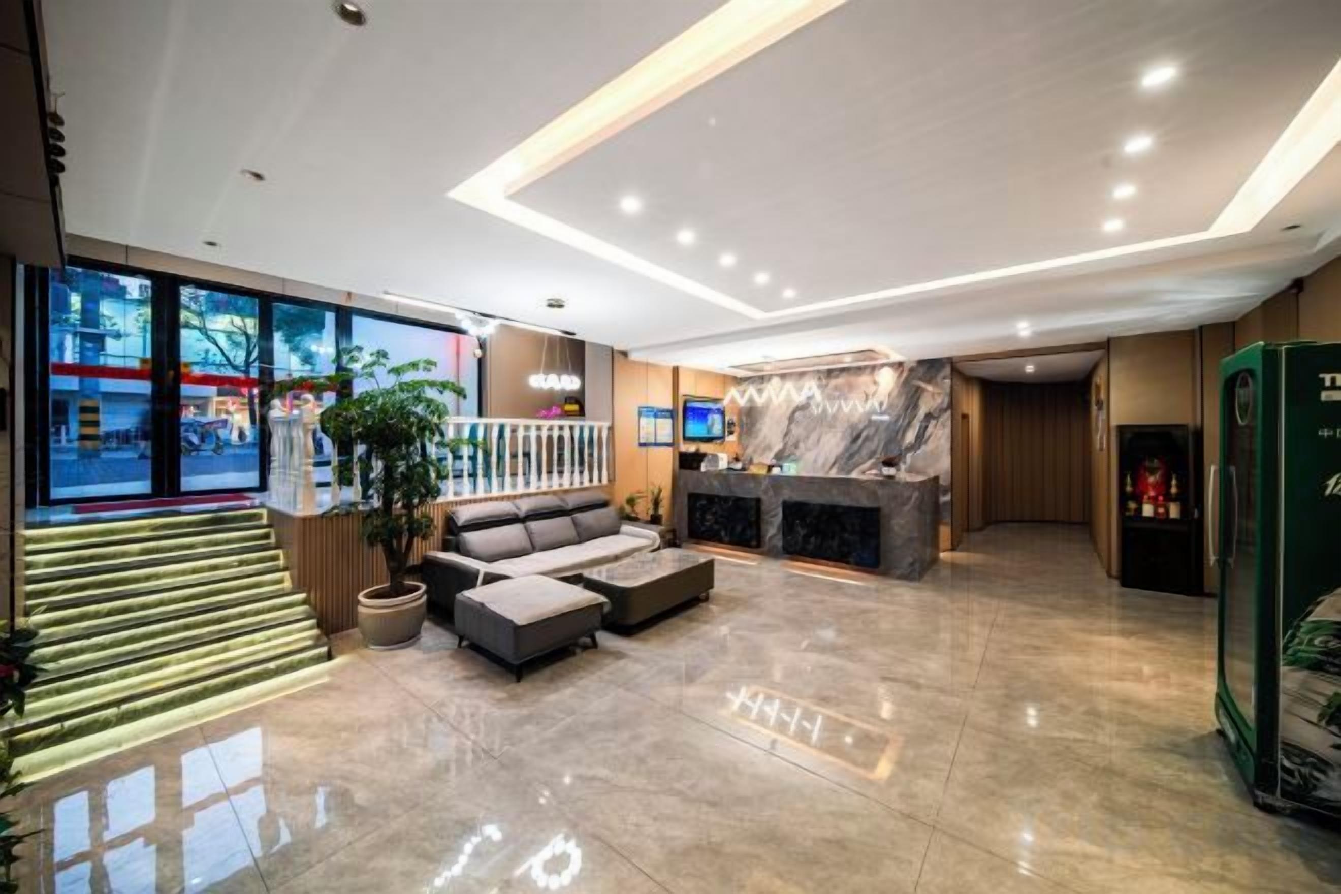 A hotel lobby with a reception desk, seating area, and a staircase.
