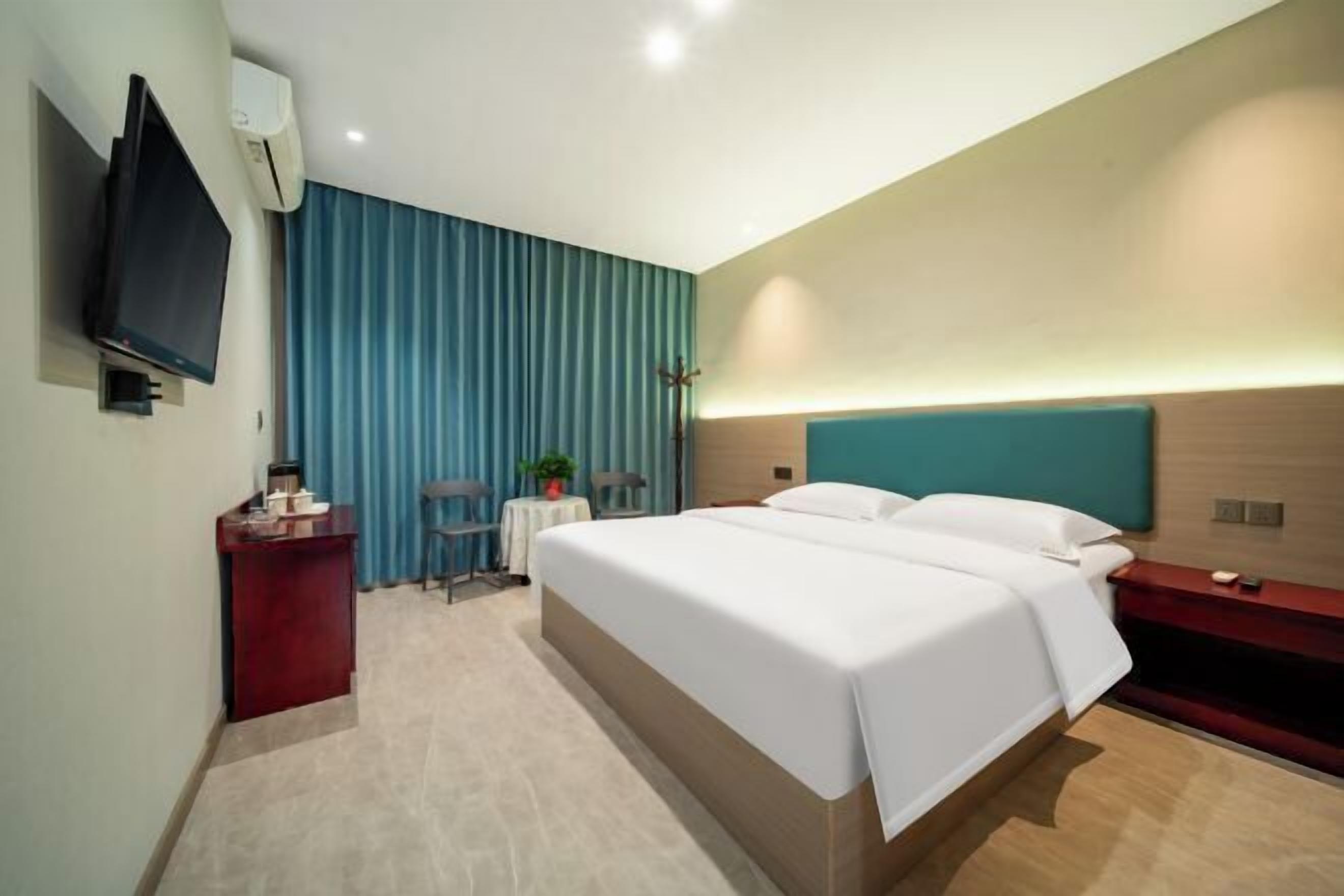 A modern hotel room with a large bed, a desk, a TV, and a window with curtains.