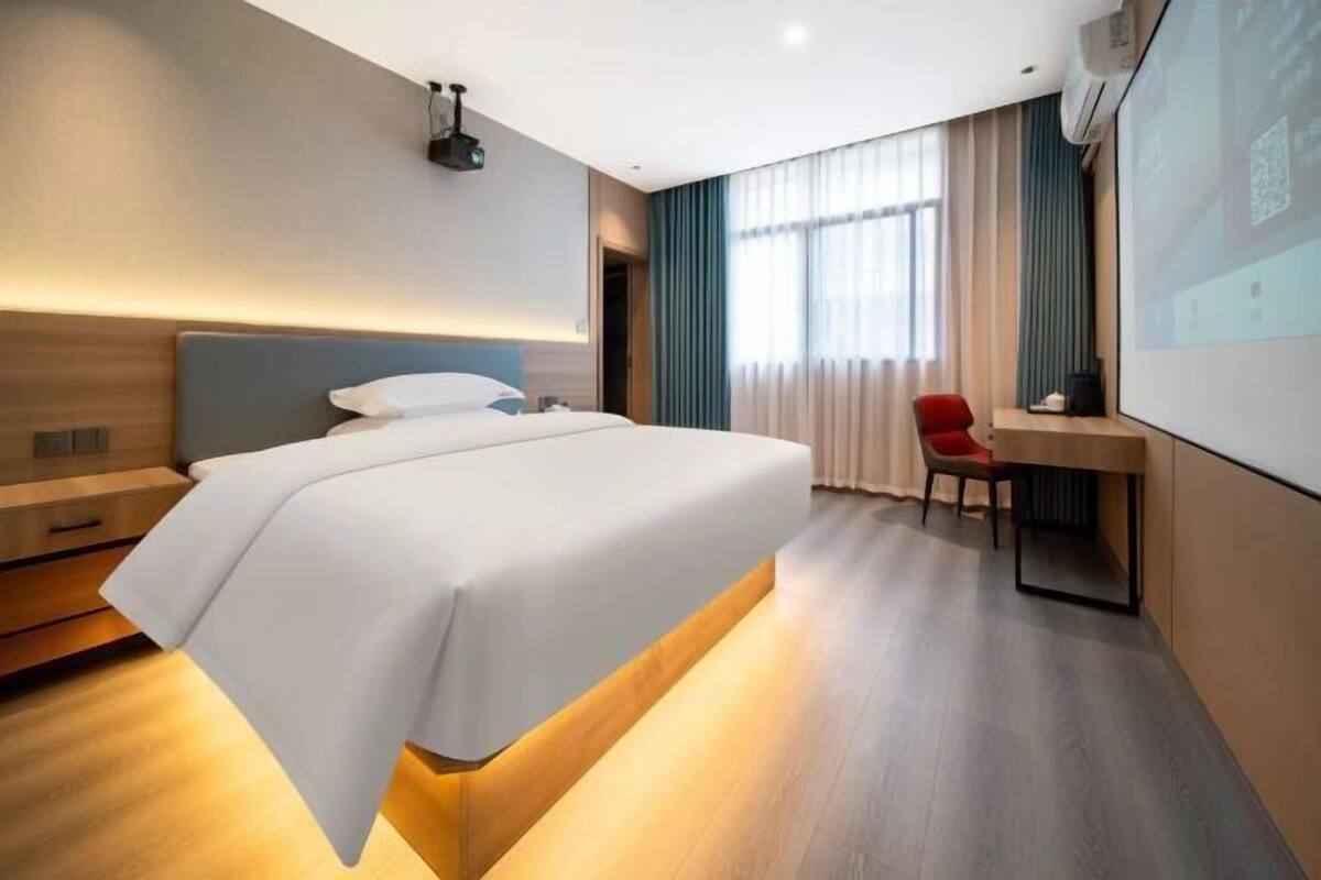 Una habitación de hotel moderna con una cama grande, un escritorio y una pantalla de proyector.