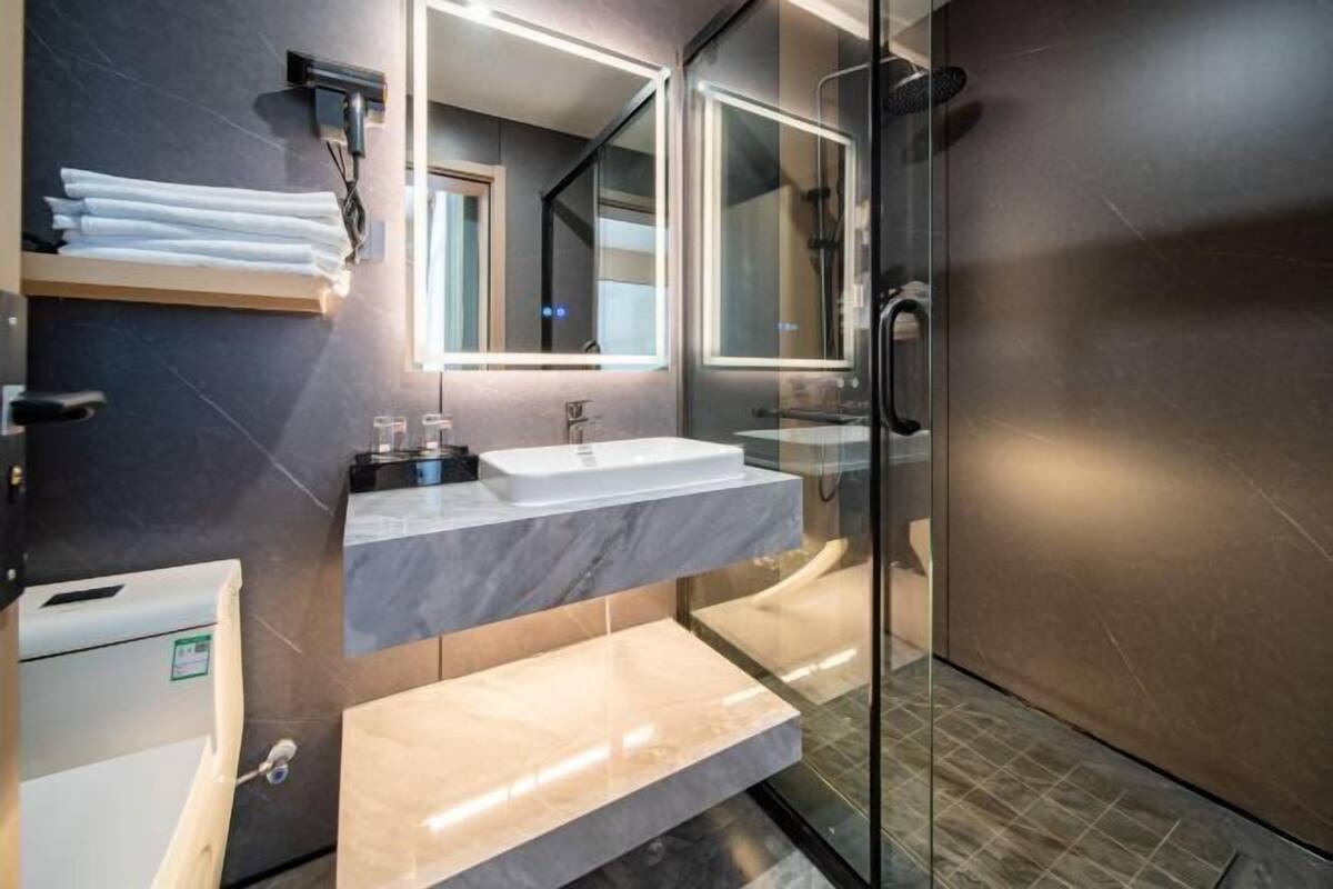 Un baño moderno con cabina de ducha de vidrio, tocador de mármol e inodoro empotrado.