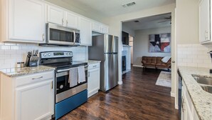 A modern kitchen with white cabinets, stainless steel appliances, and a wooden floor. - Lone Star Haven for 8 (Burleson)