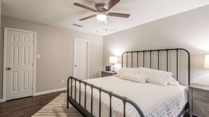 A bedroom with a bed, a nightstand, a lamp, a ceiling fan, and a door. - Lone Star Haven for 8 (Burleson)
