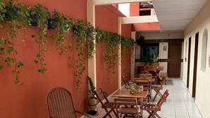 Un espacio de estar al aire libre cubierto con sillas y mesas de mimbre, piso de baldosas y una pared decorada con plantas trepadoras.