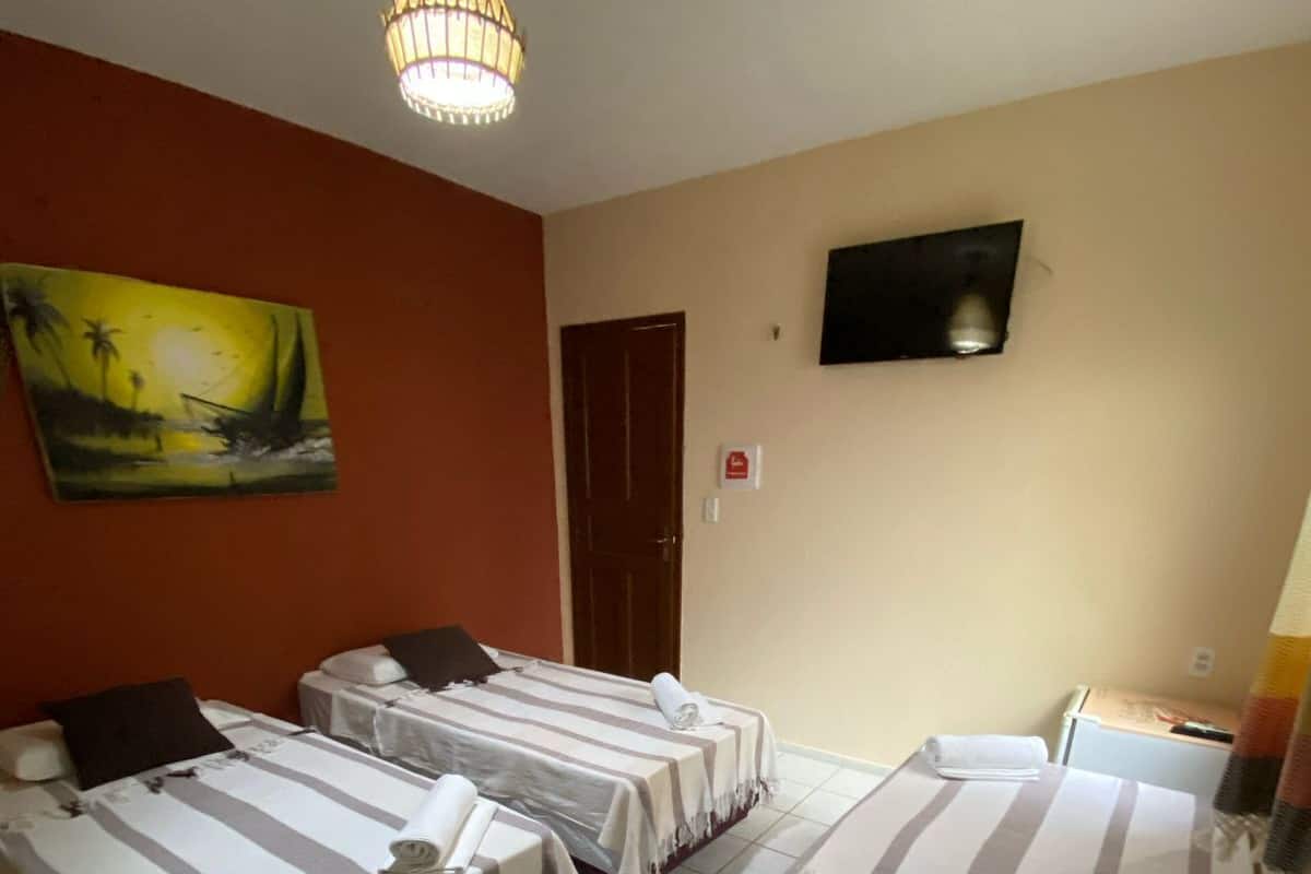 Habitación de hotel con dos camas individuales, una cama plegable y un cuadro en la pared, además de un televisor.